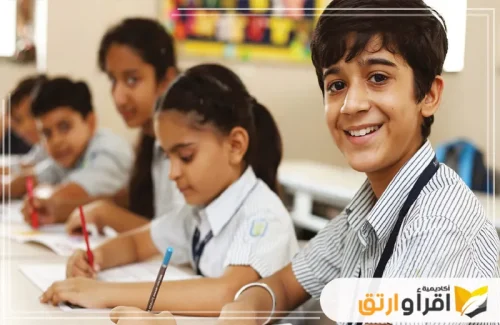 مجموعة من الطلاب يجلسون في فصل دراسي ويقومون بالكتابة. يبتسم أحدهم للكاميرا، مما يوحي ببيئة تعليمية ممتعة ومحفزة. يمكن أن تكون هذه البيئة مُعززة بـ برامج الألعاب التعليمية