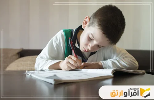 طفلًا صغيرًا يجلس على طاولة ويكتب بتركيز كبير في كراسة تحسين الخط، ويبدو أنه يستخدم كراسة تحسين الخط العربي، حيث يظهر الترتيب والتنظيم في طريقة الكتابة.