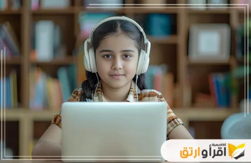 طفلة تجلس أمام جهاز كمبيوتر محمول وتضع سماعات رأس، مما يدل على تركيزها في التعلم الرقمي. تعكس هذه اللقطة سعيها نحو تحسين المستوى الدراسي من خلال الدراسة عبر الإنترنت