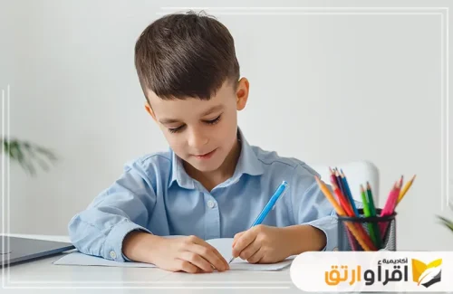 طفلًا صغيرًا يجلس بهدوء على طاولة ويركّز بانتباه أثناء الكتابة في دفتره، مما يدل على حرصه على التعلم. يمسك القلم بطريقة صحيحة ويبدو منهمكًا في تحسين الخط العربي الرقعة​