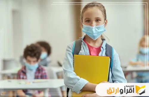 طالبة مبتسمة ترتدي قناعاً واقياً، وتحمل كتباً مدرسية، وتستعد للدخول إلى فصلها الدراسي. تعكس هذه الصورة التزام المراكز التعليمية، مثل أكاديمية اقرأ وارتق