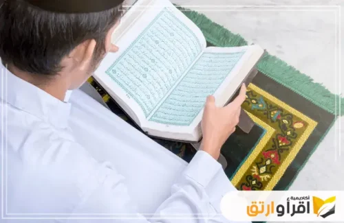 شخصًا يقرأ القرآن الكريم في جلسة هادئة على سجادة الصلاة. يظهر اهتمامه وتركيزه أثناء التلاوة. في هذا السياق، يعمل مركز تعليم القرآن للأطفال