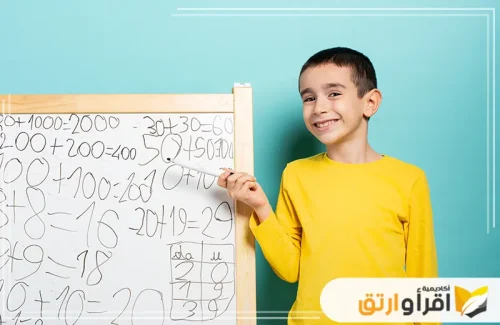 طفلًا صغيرًا مبتسمًا يقف بجانب سبورة تحتوي على مسائل رياضية مكتوبة بخط اليد. يبدو أن الطفل فخور بحل المسائل أو حيل ذكية لتحسين مهاراتك في التحد